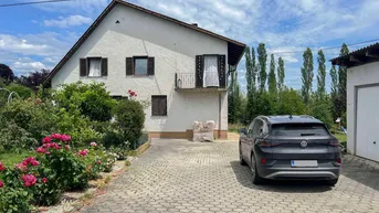 Weißes Einfamilienhaus mit Satteldach, gepflasterter Auffahrt und Vorgarten unter blauem Himmel.