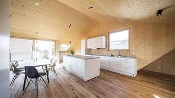 Heller offener Wohn-Essbereich mit Holzwänden, Holzboden, moderner Küche und Zugang zur Terrasse.