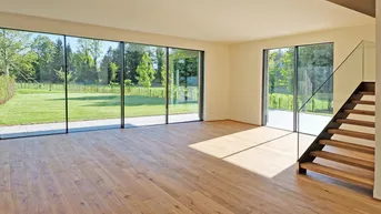 Heller, leerer Wohnbereich mit großen Fenstern, Holzboden und Blick ins Grüne, inklusive moderner Treppe.
