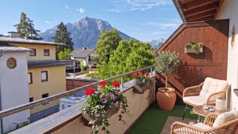 Sonniger Balkon mit Rattanmöbeln, Blumenkästen und herrlichem Bergblick in die Alpen.