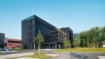 Ansicht des modernen Bürogebäudes mit dunkler Fassade und gepflegter Außenanlage unter klarem Himmel.