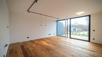 Helles, leeres Zimmer mit Holzboden und großen Fenstern, die Zugang zum Außenbereich bieten.
