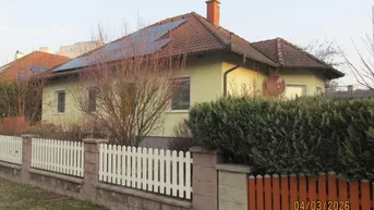 Gelbes Einfamilienhaus mit Ziegeldach, Solarpaneelen und weißem Lattenzaun im Vorgarten.