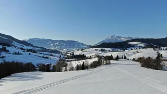 Weite, schneebedeckte Landschaft mit Bergen im Hintergrund unter blauem Himmel.