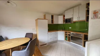 Moderne Küche mit weißen Schränken, grüner Rückwand und integriertem Essbereich.