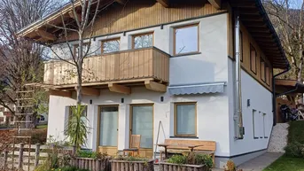 Modernes Haus mit Holzbalkonen, weißer Fassade und gepflegtem Garten in alpiner Umgebung.