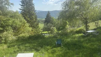 Gartenbereich mit Sitzgelegenheiten und weitem Blick über die hügelige Landschaft und Berge.