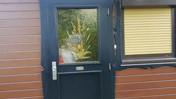 Eingangstür mit dekorativem Glas und Vordach an einer braunen Holzfassade.