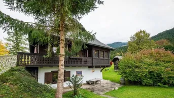 Charmantes Landhaus mit Holzbalkonen und üppiger Vegetation in bergiger Umgebung.
