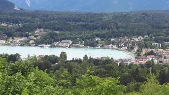 Panoramablick auf einen See mit umliegenden Häusern und bewaldeten Bergen im Hintergrund.