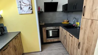 Moderne Küche mit Holzfronten, dunklen Arbeitsplatten und einer gelben Akzentwand unter Dachschräge.