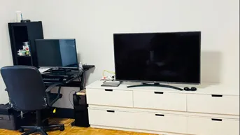 Wohnbereich mit Fernseher auf einem Sideboard und einem Arbeitsplatz mit Schreibtisch und Bürostuhl.