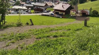 Blick auf ein malerisches Dorf in einem grünen Tal, umgeben von majestätischen Bergen unter einem teilweise bewölkten Himmel.