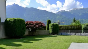 Gepflegter Gartenbereich mit Rasenfläche, hohen Hecken und beeindruckendem Bergblick im Hintergrund.