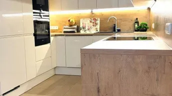 Moderne Küche mit weißen Hochglanzschränken, Holzarbeitsplatte und integrierten Geräten.