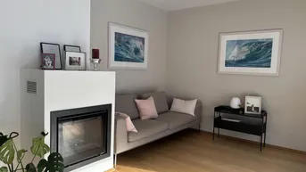 Helles Wohnzimmer mit modernem Kamin, beigem Sofa und Holzboden.