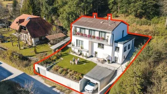 Luftaufnahme des modernen Hauses mit Garten, Garage und umliegender grüner Landschaft.