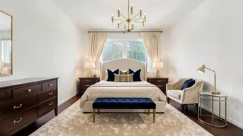 Elegantes Schlafzimmer mit dunklem Holzboden, hellem Teppich und einem großen Bett mit Samtbank.