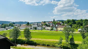 Malerischer Blick auf ein Dorf in einem grünen Tal mit Fluss und weitem Himmel.