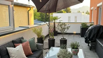 Gemütliche Dachterrasse mit Loungemöbeln, Pflanzen und stimmungsvoller Beleuchtung am Abend.