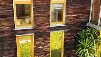Holzfassade eines modernen Gebäudes mit hohen, schmalen Fenstern und einer Pflanze im Topf.
