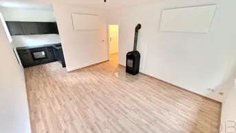 Heller offener Wohnbereich mit modernem Kaminofen und integrierter Küchenzeile, ausgestattet mit Laminatboden.