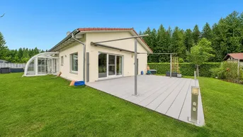Modernes Einfamilienhaus mit großer Holzterrasse, Garten und angrenzendem Wintergarten.