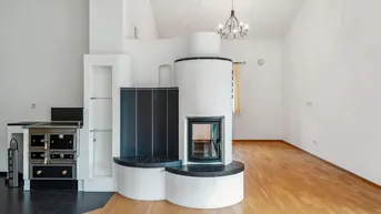 Gemütlicher Wohnbereich mit traditionellem Kachelofen und Holzboden unter hohen Decken.