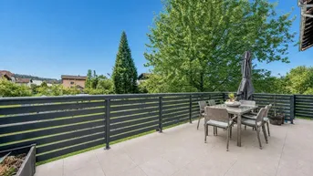 Geräumige Terrasse mit modernen Fliesen, Esstisch und Blick ins Grüne unter blauem Himmel.