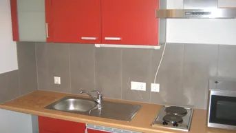 Kleine Küchenzeile mit roten Schränken, Holztheke und integriertem Spülbecken und Kochfeld.