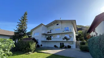 Mehrstöckiges Wohngebäude mit mehreren Balkonen, umgeben von Grünflächen und einer Auffahrt.