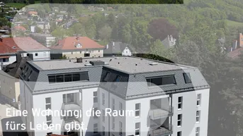 Modernes Mehrfamilienhaus mit Balkonen und Mansarddach in grüner Hügellandschaft mit Bergblick.