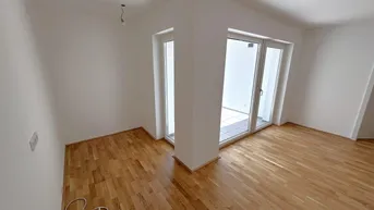 Helles Zimmer mit Parkettboden und Zugang zu einem Außenbereich durch große Glastüren.