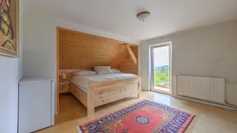 Schlafzimmer im Dachgeschoss mit Holzbett, Teppich und Zugang zu einem Balkon mit Bergblick.