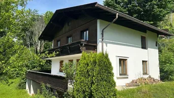 Traditionelles Haus mit weißer Fassade und dunklen Holzelementen, umgeben von üppigem Grün.