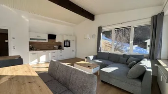 Offener Wohnbereich mit integrierter Küche, modernem Sofa und Blick auf die winterliche Landschaft.