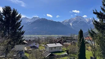 Weitläufiger Panoramablick über ein Tal mit Häusern und schneebedeckten Bergen im Hintergrund.