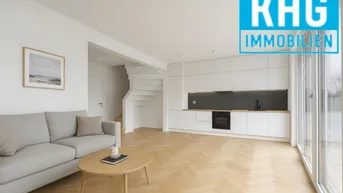 Helles, offenes Wohnzimmer mit integrierter Küche, Parkettboden und Zugang zu großen Fenstern.