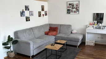 Gemütliches Wohnzimmer mit grauem Ecksofa, Holzboden und heller Wandgestaltung.