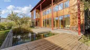 Modernes Holzhaus mit großen Glasfronten, umgeben von einem Teich und einer Holzterrasse.
