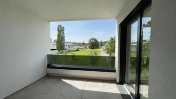 Geräumiger Balkon mit Fliesenboden, Glasbrüstung und weitem Blick ins Grüne.