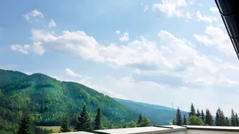 Weitläufiger Blick von einem Balkon auf die umliegende Berglandschaft unter blauem Himmel.