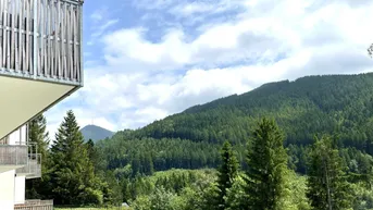 Panoramablick vom Balkon auf die umliegende Berglandschaft und dichte Wälder unter blauem Himmel.