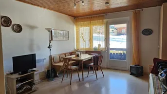 Gemütlicher Wohn- und Essbereich mit Holzbalkendecke, Parkettboden und Zugang zum Balkon.