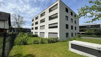 Modernes Mehrfamilienhaus mit heller Fassade und gepflegter Grünfläche unter blauem Himmel.