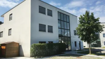 Modernes Gebäude mit klarer Architektur, großen Fenstern und gepflegter Außenanlage.