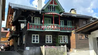 Traditionelles Holzhaus im alpinen Stil mit farbenfrohem Balkon und Giebeldach unter blauem Himmel.