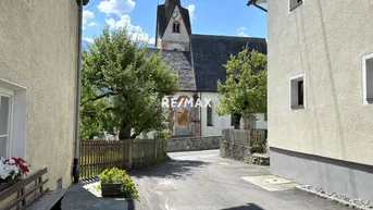 Malerische Gasse mit Blick auf eine historische Kirche und grüne Bäume unter blauem Himmel.