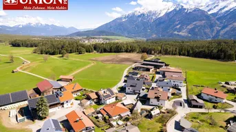 Luftaufnahme eines Dorfes mit Häusern, Feldern und majestätischen Bergen im Hintergrund.