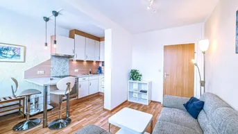 Helles Wohnzimmer mit offener Küche, Parkettboden und gemütlichem Sofa in einem kombinierten Bereich.